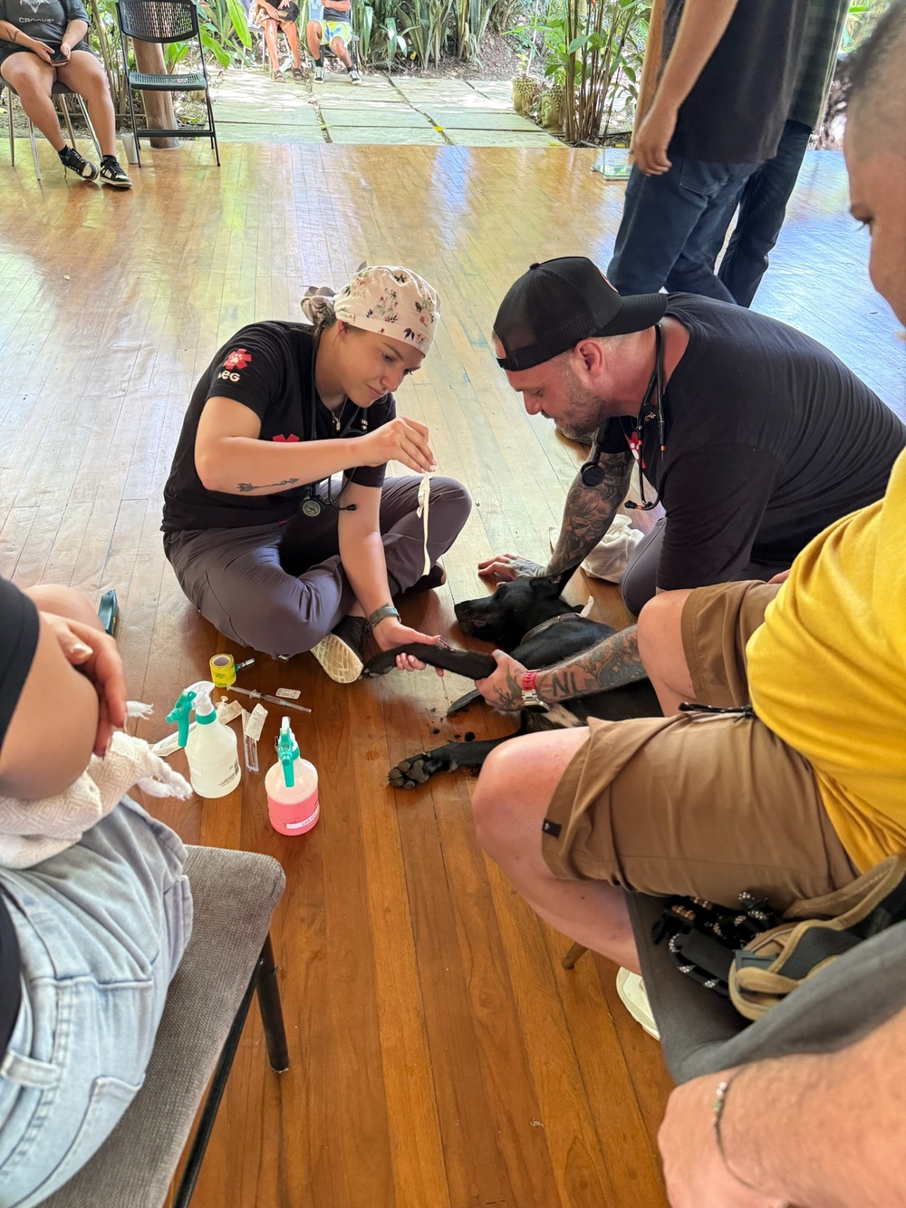 Two PRCP team members kneel on the clinic floor to treat a small black cat surrounded by medical supplies
